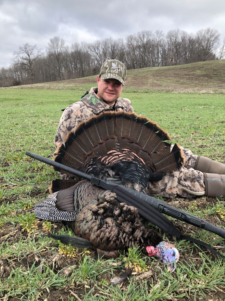 Jeremy Davis poses in camouflage with the turkey he shot on his hunt.