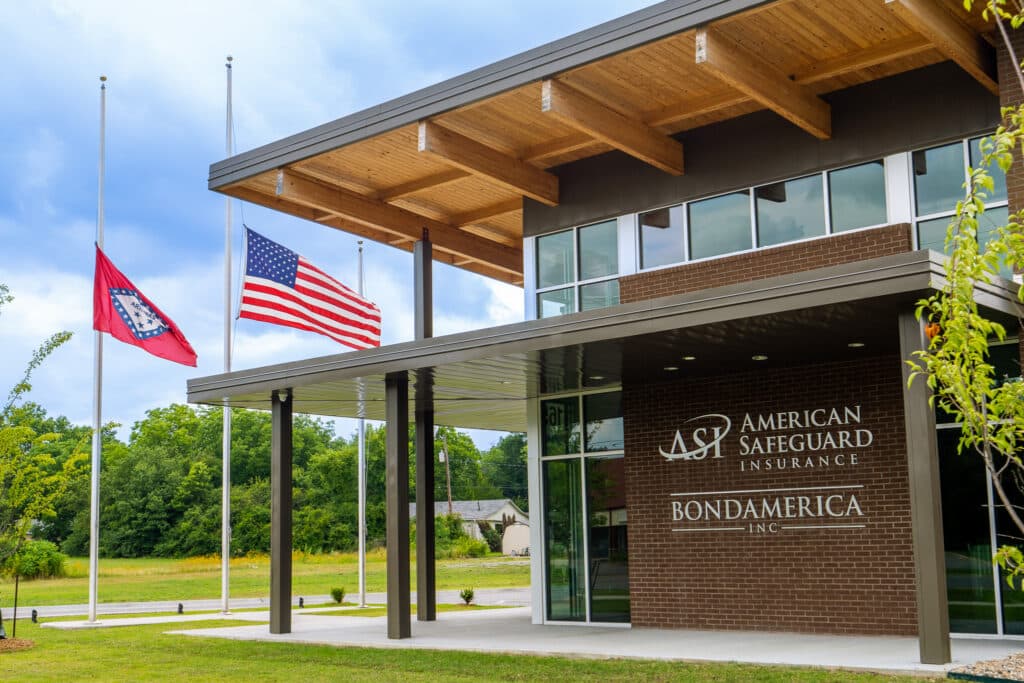 American Safeguard Insurance building exterior with logo on brick siding and Arkansas State and American flag flying.
